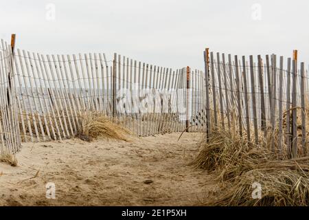 Salisbury Beach, Massachusetts - EIN sandiger Weg mit Draht und Holz Sturmzäune gesäumt führt zum Strand über der Sanddüne an einem bewölkten Wintertag. Stockfoto