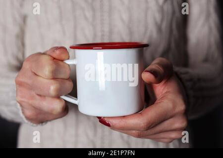 Frau Hände halten einen Retro-Topf mit einem heißen Getränk und Mädchen tragen einen Winter Wollpullover. Platz für Design oder Text kopieren Stockfoto