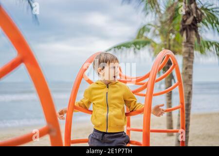 Der Junge klettert auf dem Spielplatz vor dem Hintergrund von Palmen Stockfoto