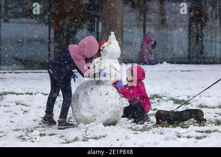 Madrid, Spanien - 08. Januar 2021: Kinder, die mit Schnee spielen und Schneemänner machen, im Buen Retiro Park in Madrid, mitten in einem verschneiten Tag, fällig Stockfoto