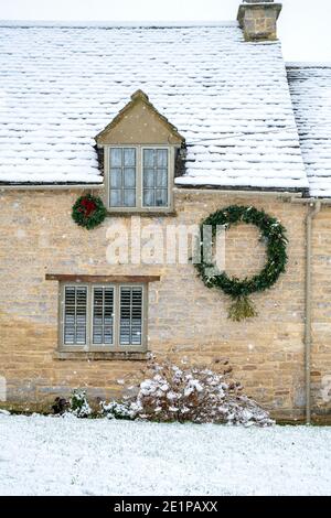 Cotswold Steinhaus mit weihnachtskranz im Dezember Schnee. Taynton, Cotswolds, Oxfordshire, England Stockfoto