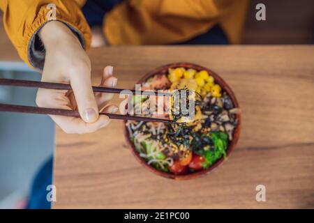 Frau, die rohe Bio-Poke-Schale mit Reis und Gemüse aus nächster Nähe auf dem Tisch isst. Draufsicht von oben horizontal Stockfoto