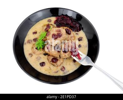 Fleischbällchen im schwedischen Stil in cremiger Sauce mit Preiselbeeren und Cranberry-Sauce in einer schwarzen Schüssel isoliert auf einem weißen Hintergrund Stockfoto