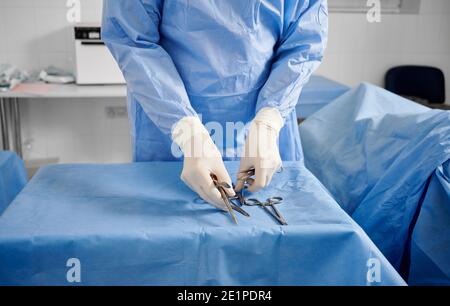 Nahaufnahme eines plastischen Chirurgen in sterilen Handschuhen, die medizinische Instrumente überprüfen. Arzt bereitet Scheren, Pinzetten und Skalpelle für die Operation vor. Konzept der plastischen Chirurgie Vorbereitung. Stockfoto