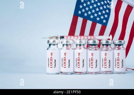 COVID-19-Impffläschchen gegen US-Flagge auf blauem Hintergrund mit Texthintergrund - Impfdosen für Coronavirus, USA-Impfkonzept. Selektiv Stockfoto