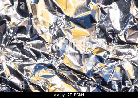 Abstrakter Hintergrund mit zerknitterter Folienstruktur, silbernen und gelben Farben. Stockfoto