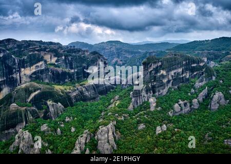 Blick über beeindruckende Säulen aus Sedimentgesteinen im ikonischen Meteora-Tal am bewölkten Frühlingstag. Hügel mit Bäumen bedeckt, kurvenreiche Straßen, Griechenland Stockfoto