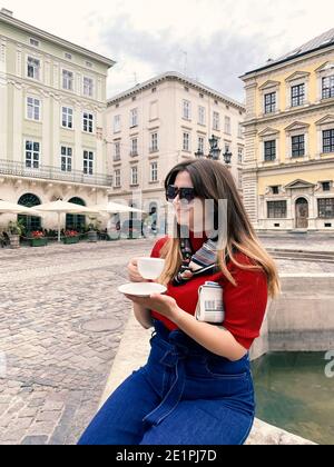 Nahaufnahme einer schönen jungen Frau, die in der Nähe des Brunnens im historischen Stadtzentrum sitzt und ihre morgendliche Tasse Kaffee genießt. Lokaler Tourismus und Stockfoto