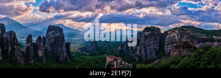 Panorama von Meteora, Griechenland, Tal und Berge bei Sonnenuntergang. Sonnenstrahlen, Hügel, Dörfer von Kalampaka und Kastraki, große Wolken. UNESCO-Weltkulturerbe Stockfoto