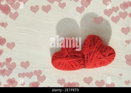 Zwei rote Herzen handgefertigt aus Wollfäden auf einem hellen Holzhintergrund. Hochwertige Fotos Stockfoto