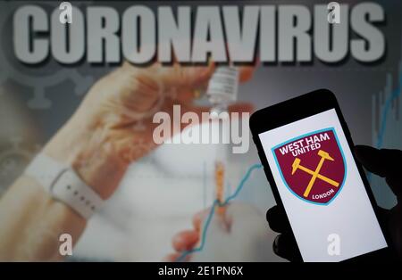 Das Logo des West Ham United Football Club wird auf angezeigt Ein Mobiltelefon mit Coronavirus-Illustration auf einem Monitor Im Hintergrund Stockfoto