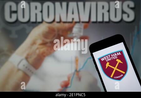 Das Logo des West Ham United Football Club wird auf angezeigt Ein Mobiltelefon mit Coronavirus-Illustration auf einem Monitor Im Hintergrund Stockfoto