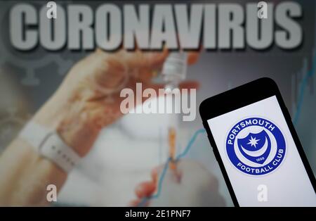 Das Logo des Portsmouth Football Club wird auf einem Handy angezeigt Telefon mit einer Coronavirus-Abbildung auf einem Monitor im Hintergrund Stockfoto