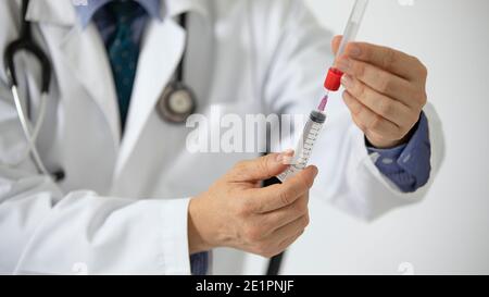 Ein Arzt im weißen Mantel, der mit einer Spritze eine Probe aus einem Blutröhrchen zieht. Stockfoto