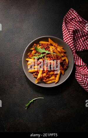 Blick von oben auf Penne Pasta mit Bolognese Sauce auf dunkel Oberfläche Stockfoto