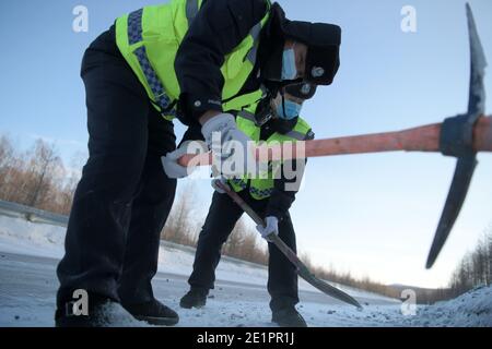 Dahinggan, Chinas Provinz Heilongjiang. Januar 2021. Der Verkehrspolizist Sun Chen (vorne) und sein Kollege deice eine Straße im Bezirk Huzhong in Dahinggan, nordöstlich der Provinz Heilongjiang, 8. Januar 2021. Sun Chen ist seit 35 Jahren Verkehrspolizist. Im Bezirk Huzhong, genannt "die kälteste Stadt Chinas", klebte Sun an seinem Posten, um die Verkehrsordnung aufrechtzuerhalten. Trotz des extrem kalten Wetters mit der niedrigsten Temperatur von etwa minus 40 Grad Celsius nahm er früh am Morgen seine Schicht auf. Quelle: Wang Jianwei/Xinhua/Alamy Live News Stockfoto