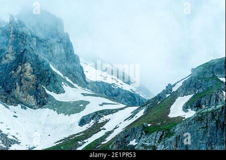 Schlechtes Wetter in den Bergen. Wolken kommen aus dem Tal und verdunkeln den Himmel. Auf den Pisten bleiben noch ein paar Schneepatchen. Stockfoto