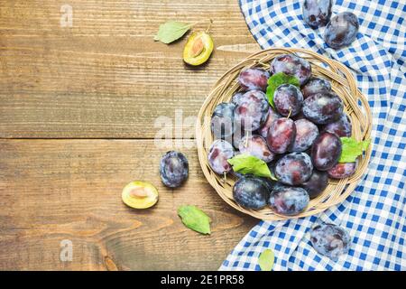 Viele frische Bio-Pflaumen in Holzkorb mit Blättern, Draufsicht mit Platz für Text. Gesunde Früchte. Stockfoto