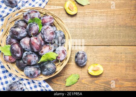 Viele frische Bio-Pflaumen in Holzkorb mit Blättern, Draufsicht mit Platz für Text. Gesunde Früchte. Stockfoto