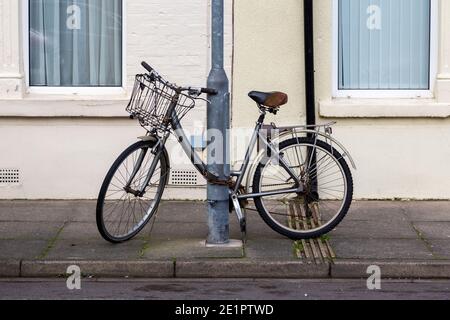 Ein altes Damenfahrrad mit einem Korb, der an einem angekettet ist lamppost in der Straße Stockfoto