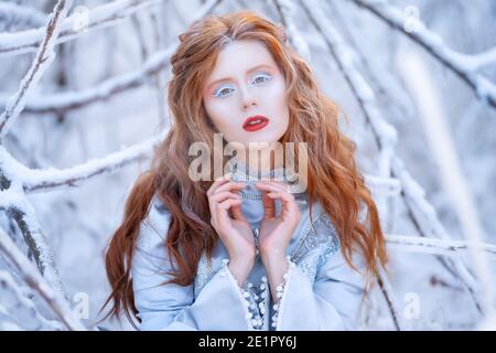 Junge Rotschopf Frau, eine Prinzessin, Spaziergänge in einem Winterwald in einem blauen Kleid. Stockfoto