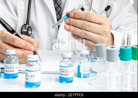 Ein Arzt mit einer Glasspritze, der das Testergebnis schreibt Auf einem Notizbuch mit mehr Fläschchen mit Covid-19-Impfstoff und Einige Reagenzgläser in einem Rack auf einem WH Stockfoto