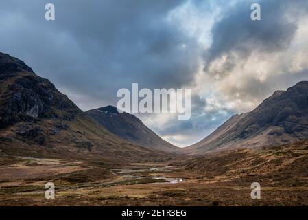 Atemberaubende Landschaftsaufnahme im Glencoe Valley in den schottischen Highlands Mit Bergketten in dramatischer Winterbeleuchtung Stockfoto