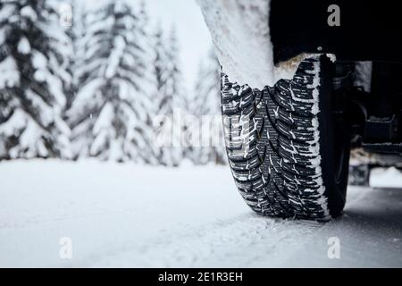 Nahaufnahme des Autoreifens auf schneebedeckter und vereister Straße. Themen Sicherheit und Fahren im Winter. Stockfoto