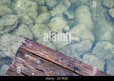 Blick auf den Boden eines flachen Teiches mit Steinen Und eine Holzterrasse Stockfoto