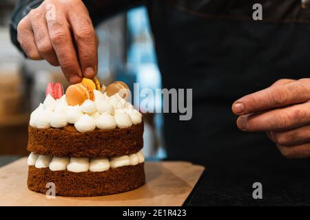 Nahaufnahme der Hände eines Bäckers, die einen Kuchen mit Makronen dekorieren Stockfoto