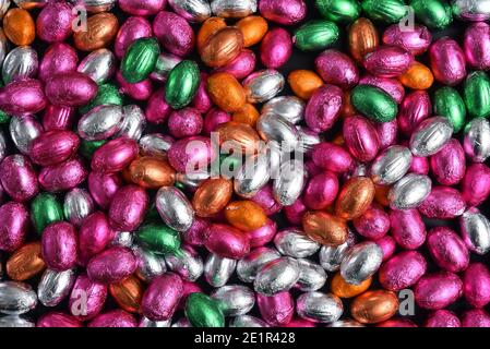 Rosa, grün, orange, silber und Bronze Folie verpackt Schokolade ostereier, vor einem schwarzen Hintergrund. Stockfoto