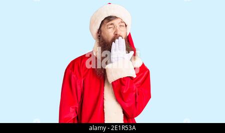 Schöner junger Mann mit rotem Kopf mit langem Bart trägt weihnachtsmann Kostüm gelangweilt gähnend müde Abdeckung Mund mit der Hand. Unruhig und Schläfrigkeit. Stockfoto