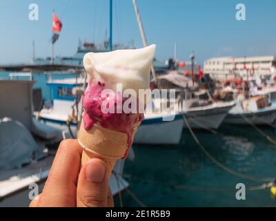 Eis in der Hand schmelzen gegenüber den Booten am Yachthafen. Heißes Sommerkonzept. Kaltes Eis während der Sommerhitze Stockfoto