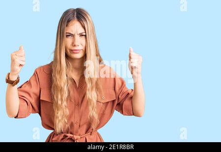 Schöne kaukasische Frau mit blonden Haaren tragen Sommer Jumpsuit wütend und verrückt Heben Fäuste frustriert und wütend während schreien vor Wut. Wut Stockfoto