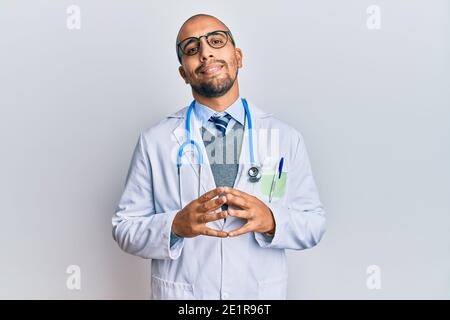 Hispanic erwachsenen Mann trägt Arzt Uniform und Stethoskop Hände zusammen und die Daumen überquert lächelnd entspannt und fröhlich. Erfolg und optimistisch Stockfoto
