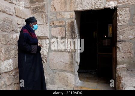 Äthiopisch-orthodoxer Priester mit Gesichtsmaske aufgrund der Covid-19-Pandemie steht am Eingang zur koptischen Kapelle des Erzengels St. Michael im unteren Teil des Klosters Deir El-Sultan im Komplex der Grabeskirche in der Altstadt von Jerusalem Israel Stockfoto