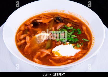 Traditionelle russische Suppe Soljanka gekocht mit Fleisch, Wurst, gesalzene Gurken und Oliven mit Kräutern bestreut und gewürzt mit saurer Sahne. Stockfoto