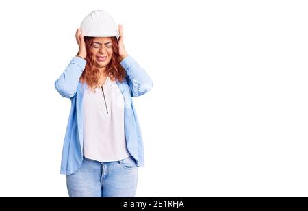 Junge lateinische Frau trägt Architekt Hardhat leiden unter Kopfschmerzen verzweifelt und gestresst, weil Schmerzen und Migräne. Hände auf dem Kopf. Stockfoto