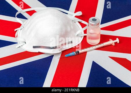 Großbritannien Flagge, n95 Gesichtsmaske, Nadelspritze und Fläschchen. Konzept der britischen Covid-19 Coronavirus-Impfstoffverteilung, Versorgungsengpässe und Gesundheitsversorgung c Stockfoto