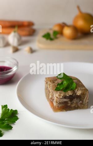 Ein Stück Gelees mit Petersilie auf einem weißen Teller. Festliche Gerichte. Traditionelles Essen. Speicherplatz kopieren. Stockfoto