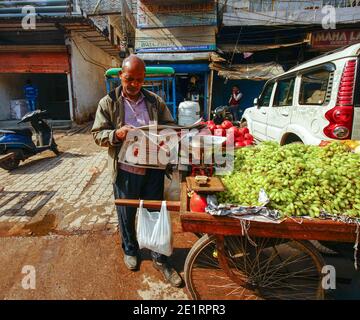 02-07-2019 Delhi, Indien. Mann liest Zeitung und Verkauf von leckeren Trauben (ohne Samen). Sonniger Tag Stockfoto