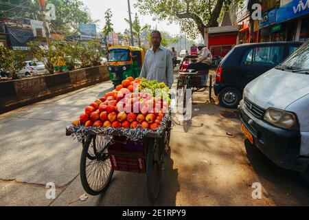 02-07-2019 Delhi, Indien. Der Mensch und sein Obstwagen (Äpfel Trauben Orangen). Ein Tuk-Tuk Auto fährt von hinten (Main Bazar Rd.) Stockfoto