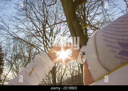 Sonnenlicht umgeben von einem mit meinen Händen geschaffenen Herzen, im Hintergrund ein Wald im Schatten des Winterlichts Stockfoto