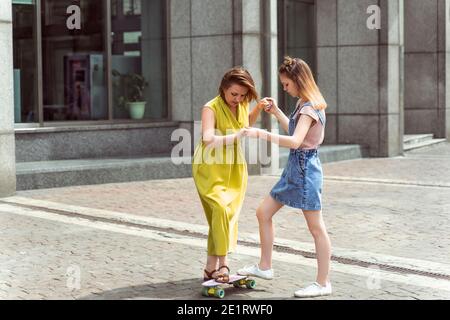 Kaukasische Teenager-Mädchen lehrt ihre Mutter, wie man Skate. Outdoor Lifestyle Bild an einem sonnigen Sommertag. Stockfoto