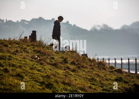 Heysham, Lancashire, Unite Kingdom 9. Januar 2021 Dog Walker Walkers her walkers her down a grassy Bank on to Heysham Promenade Diuring the Second Week End Covid Restriction Credit: PN News/Alamy Live News Stockfoto