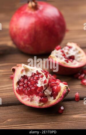 Frische, reife, saftige Granatapfelfrucht wird auf braunem Holzhintergrund in Stücke geteilt. Stockfoto