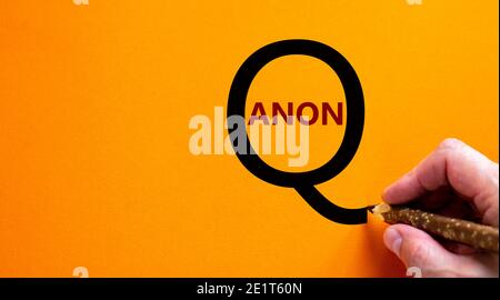 Q Anon-Symbol. Handschriftliche Worte 'Q Anon', isoliert auf schönem orangefarbenen Hintergrund. Business- und q Anon-Konzept, Kopierbereich. Stockfoto