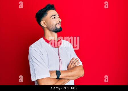 Junger Mann mit Bart Musik hören mit Kopfhörer suchen Zur Seite mit gekreuzten Armen überzeugt und selbstbewusst Stockfoto