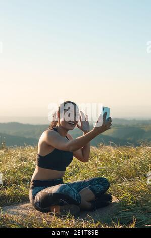 Eine fröhliche junge Frau in Sportkleidung mit Video-Chat im Freien, lächelnd und winkend Stockfoto