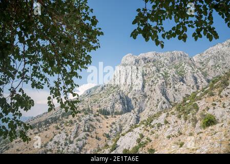 Gebadet in Sonnenlicht, umgeben mittelalterliche Kotor Festung, wie von einem Bergpfad hinter der antiken Stadt gesehen. Stockfoto